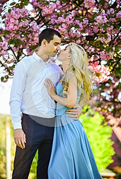 Romantic couple under sakura tree. couple in love kiss and embrace. spring flower bloom. man and woman in park with pink