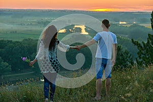 Romantic couple walk on hill at sunset on country outdoor, girl with bouquet of wild flower, beautiful landscape and bright yellow