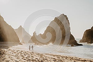 Romantic couple walking along coastline at Ursa Beach among beautiful rocks on sunset. Silhouette Shot. Back view