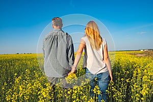 Romantic couple is walking through the field of yellow flowers