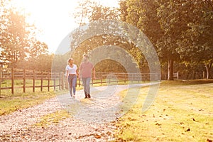 Romantic Couple Walking Hand In Hand Along Country Lane At Sunset