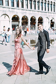 Romantic couple walking on Piazza San Marco in Venice. Pretty girl in pink dress and handsome boy in black clothes