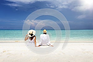 A romantic couple in white summer clothes sits hugging on a tropical beach