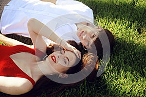 Romantic couple of young people lying on grass in park. Happy Couple Relaxing on Green Grass. Park. A girl in a beautiful dress