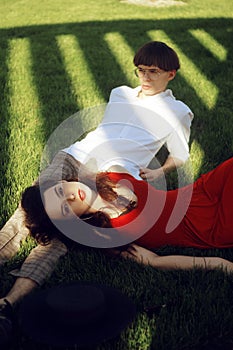 Romantic couple of young people lying on grass in park. Happy Couple Relaxing on Green Grass. Park. A girl in a beautiful dress