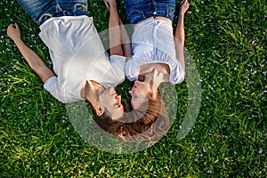 Romantic couple of young people lying on grass in park. They lay on the shoulders of each other and hold hands together