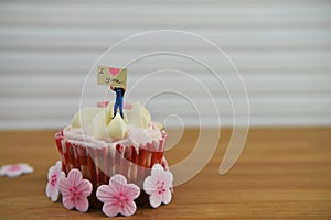 Romantic cup cake in pink and white with miniature person figurine on top holding a sign board