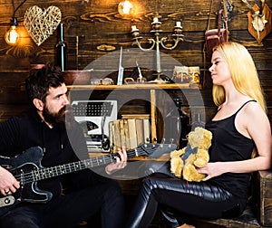 Romantic date concept. Couple in love on relaxed faces enjoy romantic atmosphere. Man play guitar while lady holds teddy