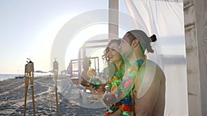 Romantic date of couple what seated on beach, male sits near to girl and points hand into distance,