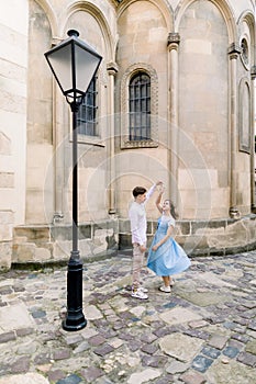 Romantic date and dance outdoor in the city. Happy young couple, man in white shirt and charming girl in blue dress