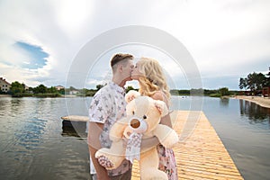 Romantic date surprise. A young guy and a girl on a pier overlooking the lake. The guy gives the girl a teddy bear