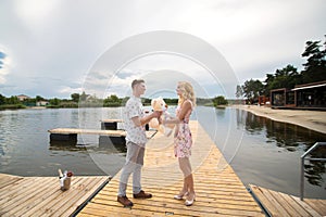 Romantic date surprise. A young guy and a girl on a pier overlooking the lake. The guy gives the girl a teddy bear