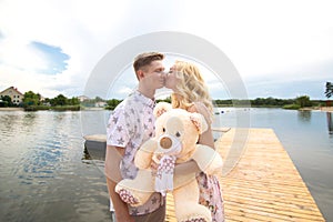 Romantic date surprise. A young guy and a girl on a pier overlooking the lake. The guy gives the girl a teddy bear