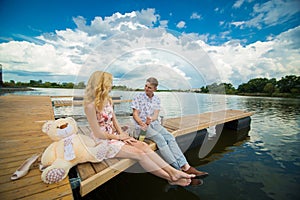 Romantic date surprise. A young guy and a girl on a wooden pier. The guy opens the champagne