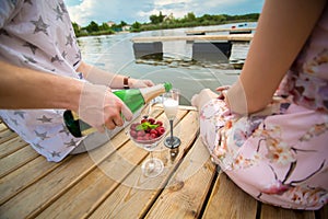 Romantic date surprise. A young guy and a girl on a wooden pier. The guy pours champagne into the glasses
