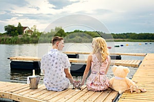 Romantic date surprise. A young guy and a girl on a wooden pier. The guy pours champagne into the glasses