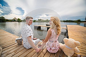 Romantic date surprise. A young guy and a girl on a wooden pier. The guy pours champagne into the glasses