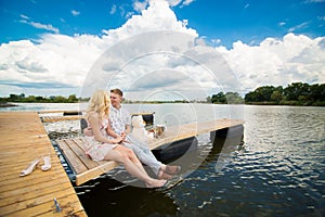 Romantic date surprise. A young guy and a girl on a wooden pier. Hug and kiss while sitting on the pier. Romantic love story