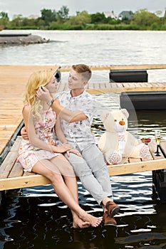 Romantic date surprise. A young guy and a girl on a wooden pier. Hug and kiss while sitting on the pier. Romantic love story