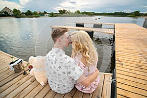 Romantic date surprise. A young guy and a girl on a wooden pier. Hug and kiss while sitting on the pier. Romantic love story