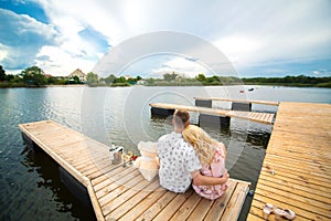 Romantic date surprise. A young guy and a girl on a wooden pier. Hug and kiss while sitting on the pier. Romantic love story