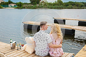 Romantic date surprise. A young guy and a girl on a wooden pier. Hug and kiss while sitting on the pier. Romantic love story