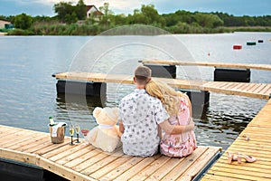 Romantic date surprise. A young guy and a girl on a wooden pier. Hug and kiss while sitting on the pier. Romantic love story