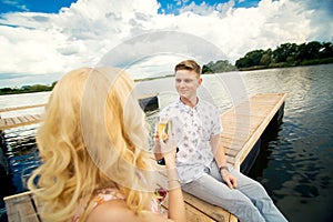 Romantic date surprise. A young guy and a girl on a wooden pier. Raise glasses with champagne