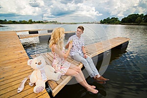 Romantic date surprise. A young guy and a girl on a wooden pier. Raise glasses with champagne