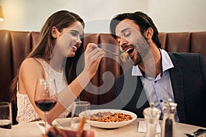 Romantic, date and woman feeding man spaghetti for dinner, supper and fine dining at a restaurant together. Couple, cute