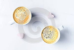 Romantic desk top with two cups of coffee and pink heart shaped marshmallows. Top view.
