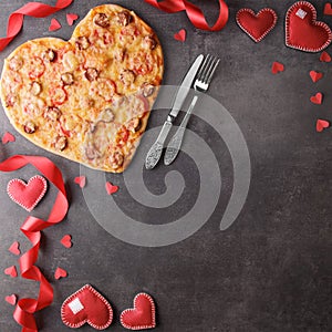 Romantic dinner. Heart shaped pepperoni pizza and bright red ribbon on dark