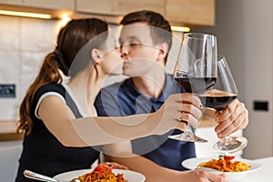 Romantic dinner at home. Happy couple kissing, clinking glasses and eating bolognese pasta with wine at kitchen. Concept