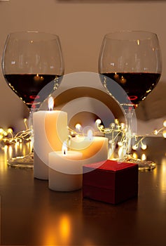 Romantic dinner scene at home: candles, box with a jewel and two glasses of wine.