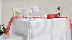 Romantic dinner table set and chair preparation with white theme decoration, white sand, clear cloudy sky, and tranquil, peaceful
