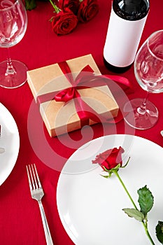 Romantic dinner table setting for Valentines Day. Rose flower on plate, gift box, bottle of win, glasses