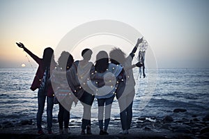 Romantic and dreamer concept image with five friends women hug each other viewed from back looking at the sunset holiding light -