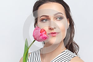 Romantic dreaming brunette woman standing looking away, holding pink tulip enjoying aromat of flower