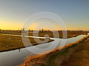 Romantic Dutch countryside amidst extensive grassy meadows and canals whose water reflects the sunset
