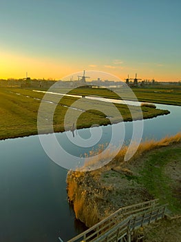 Romantic Dutch countryside amidst extensive grassy meadows and canals whose water reflects the sunset