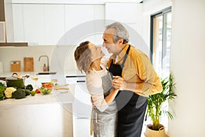 Romantic elderly man and woman dancing together at home in kitchen interior, enjoying spending time with each other