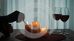 Romantic evening by candlelight. Hands of a man lighting candles with matches close up. Burning candles and glasses with