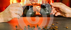 Romantic evening. Couple having a cup of coffee near the fire. Close-up of hands in the backlight of a burning fireplace