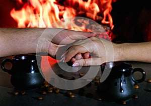 Romantic evening. Couple having a cup of coffee near the fire. Close-up of hands in the backlight of a burning fireplace