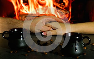 Romantic evening. Couple having a cup of coffee near the fire. Close-up of hands in the backlight of a burning fireplace