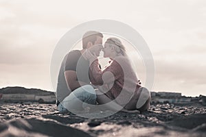 Romantic evening with girl and boy together sitting at the beach on the sand kissing in tenderness. Two people male and female in