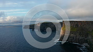 Romantic evening panoramic shot of high cliffs at sunset. Vertical rock walls above ripples sea surface. Cliffs of Moher