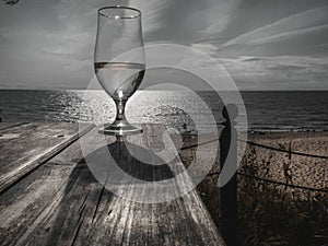 Romantic evening sunset with misty glass of white wine on background sea, on wooden table