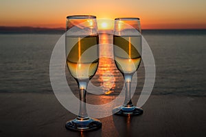 Romantic evening, sunset, two wineglasses, sun path on the water between two wineglasses with wine