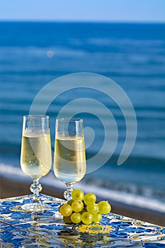 Romantic event, bottle with cold sparkling wine, cava or champagne served with two glasses on table with sea view and palm tree